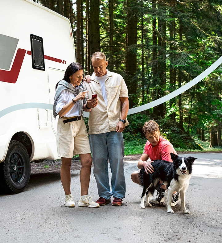 Two adults standing next to a camper van, focused on a Vasco Translator V4. Next to them, their son is gently petting a dog, capturing a peaceful family travel scene.